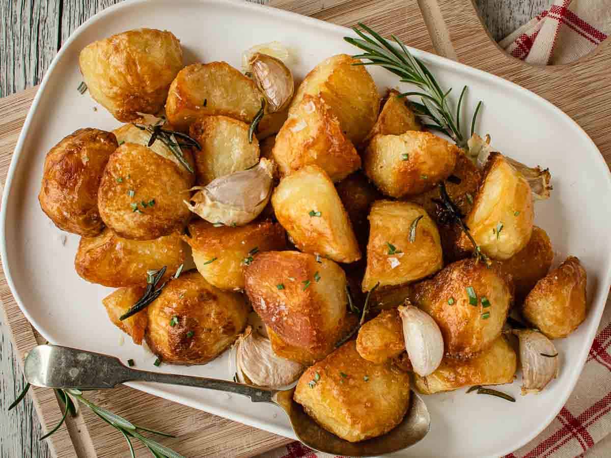 These Roasted Potatoes are crispy and crunchy. Roasted with garlic and rosemary these potatoes are the perfect side dish. #roastedpotatoes #roasted #potatoes #sides Overhead view of roasted potatoes with rosemary and garlic on a white platter.