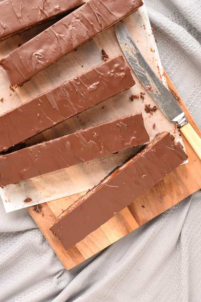 Chocolate Cherry Slice is a wonderful combination of the classic flavors of chocolate, cherry and coconut in one sweet slice. #chocolateslice #chocolatebars #chocolatecherryslice #chocolaterecipe #recipe #baking Five long slices chocolate cherry slice on a wooden board with vintage knife viewed from above