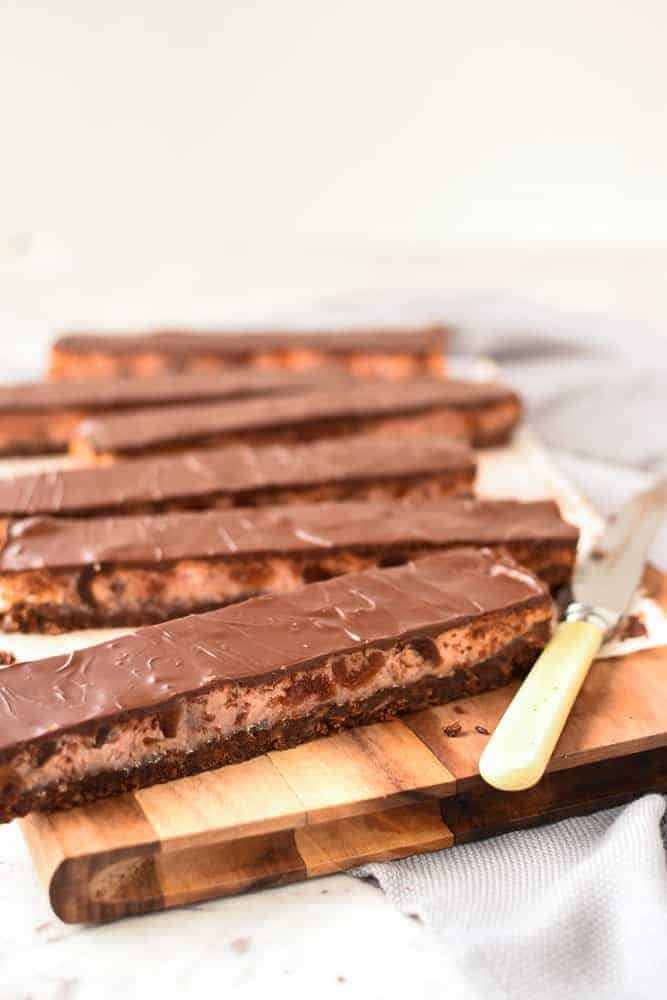 Chocolate Cherry Slice is a wonderful combination of the classic flavors of chocolate, cherry and coconut in one sweet slice. #chocolateslice #chocolatebars #chocolatecherryslice #chocolaterecipe #recipe #baking Six long slices of chocolate cherry slice on a wooden board with vintage knife viewed from 45 degree angle