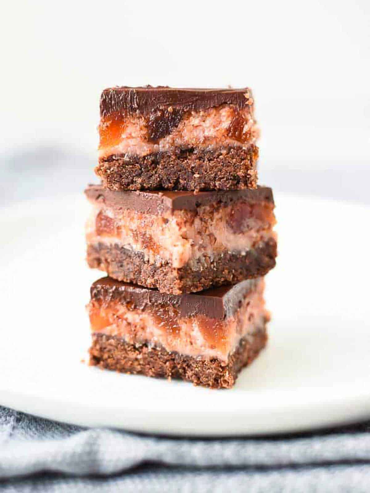 Chocolate Cherry Slice is a wonderful combination of the classic flavors of chocolate, cherry and coconut in one sweet slice. #chocolateslice #chocolatebars #chocolatecherryslice #chocolaterecipe #recipe #baking Three Cherry Ripe Bars stacked one on top of the other on a white plate viewed front on.