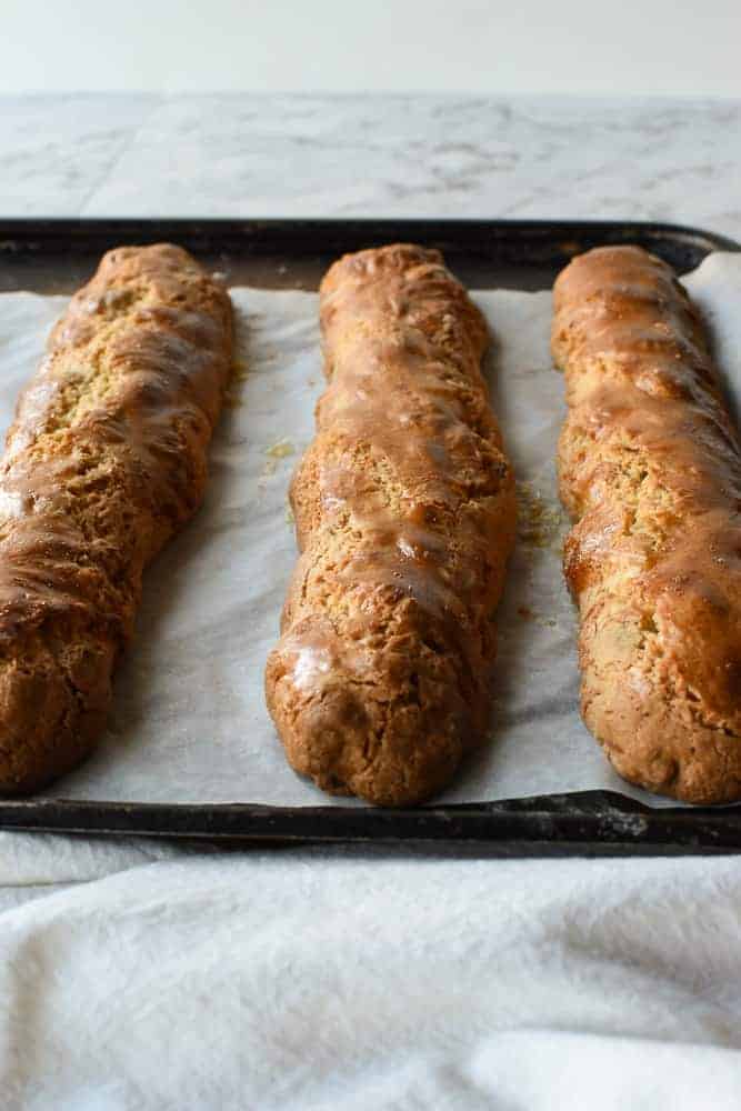 Italian Almond biscotti are easy to make at home. They are crunchy and perfect for dipping in vin santo or an espresso. #italianrecipe #almondbiscotti #italianalmondbiscotti #biscottirecipe Three baked, oblong shaped cakes on baking tray.