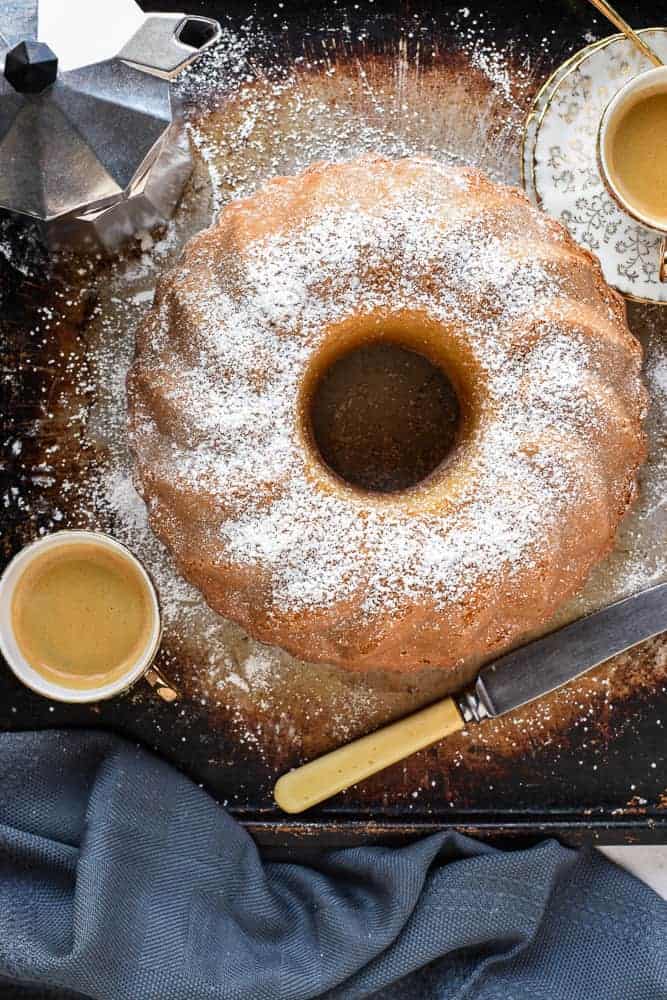 This Lemon Yogurt cake is a traditional Italian breakfast cake. Simple to make and perfect with your morning coffee. #yogurtcake #lemoncake #cakerecipe #italiancake #italianrecipe #baking this cake with knife, two espresso cups of coffee and coffee moka pot viewed from above.