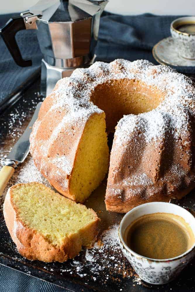 This Lemon Yogurt cake is a traditional Italian breakfast cake. Simple to make and perfect with your morning coffee. #yogurtcake #lemoncake #cakerecipe #italiancake #italianrecipe #baking Lemon Yogurt cake with slice in the front and two espresso cups of coffee and moka pot.