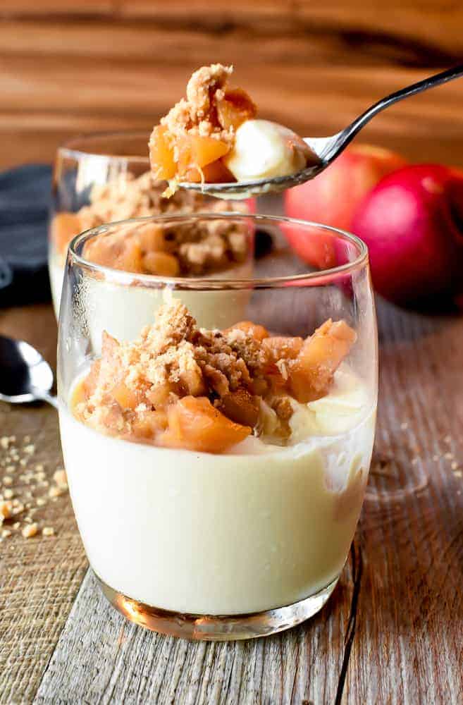 Cinnamon Panna Cotta with Apple Crumble topping makes a perfectly easy dessert that is as impressive as it is flavourful! #pannacotta #cinnamon #pannacottarecipe #italiandessert #applecrumble #applecrisp glass of panna cotta with apple crumble topping and a spoonful being removed