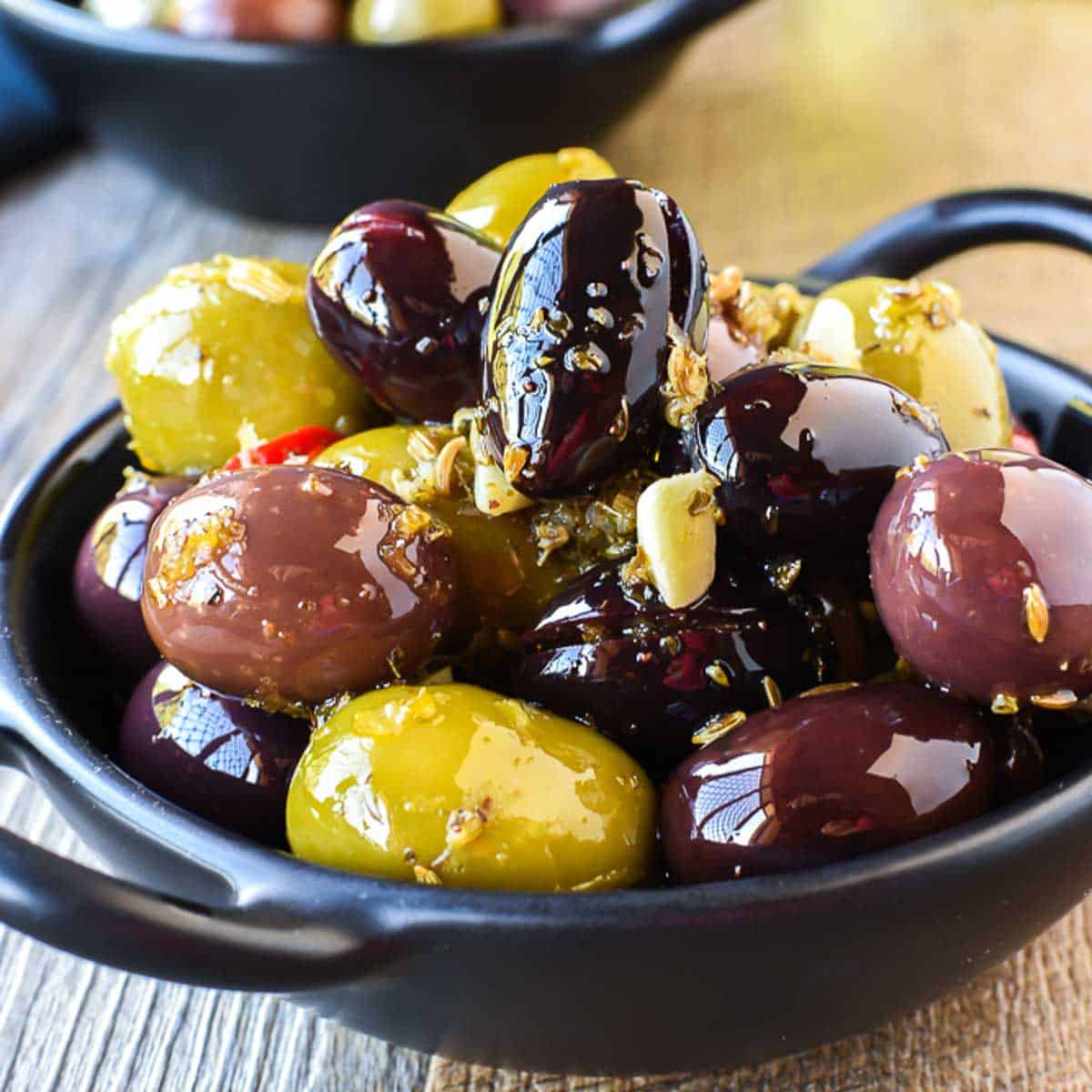 two black bowls filled with assorted olives viewed front on