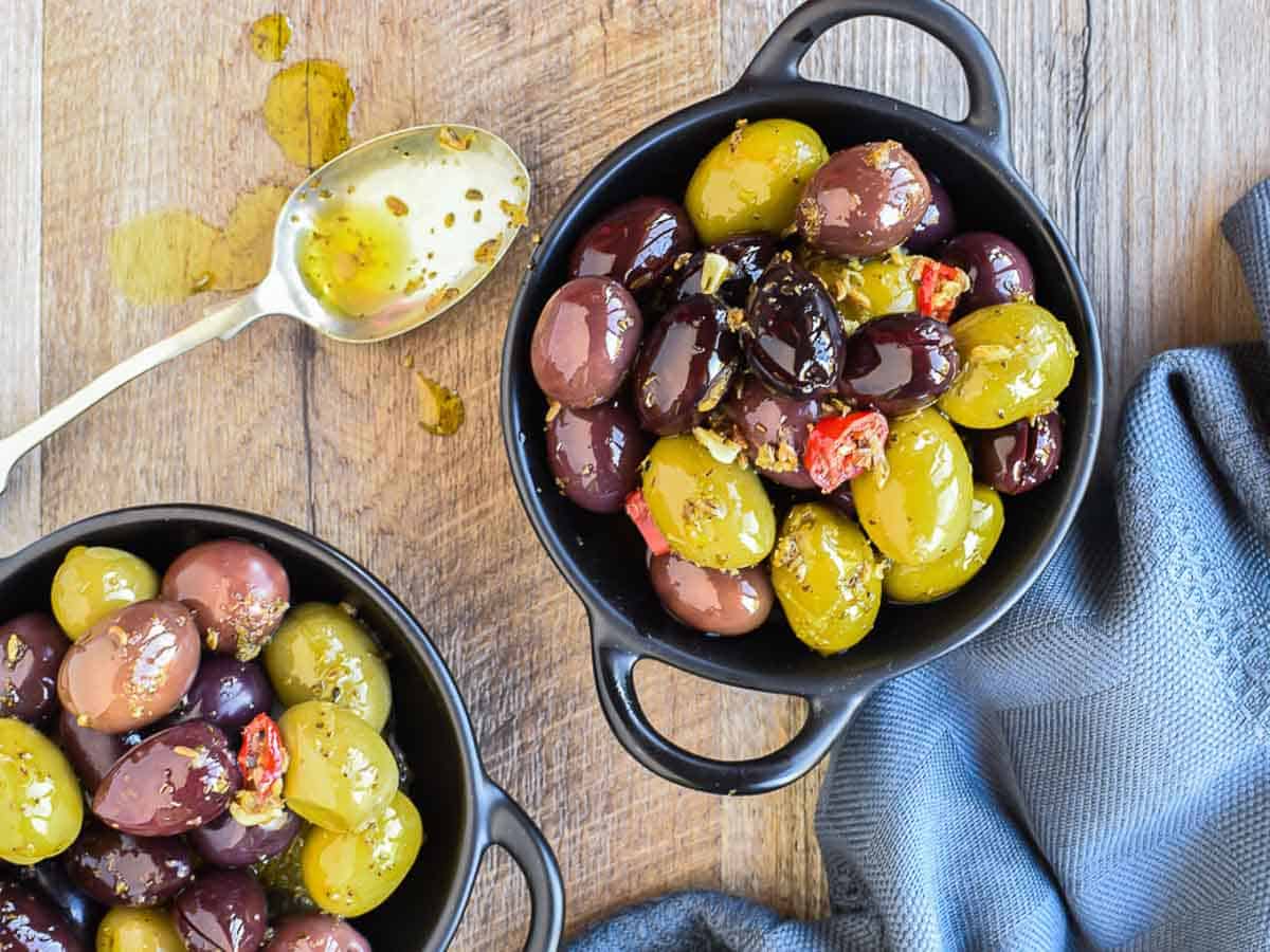 Two black bowls with assorted olives and spoon viewed from above.