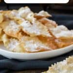 Plate of fried Italian pastry - crostoli dusted with powdered sugar. One crostolo crumbled at the front.