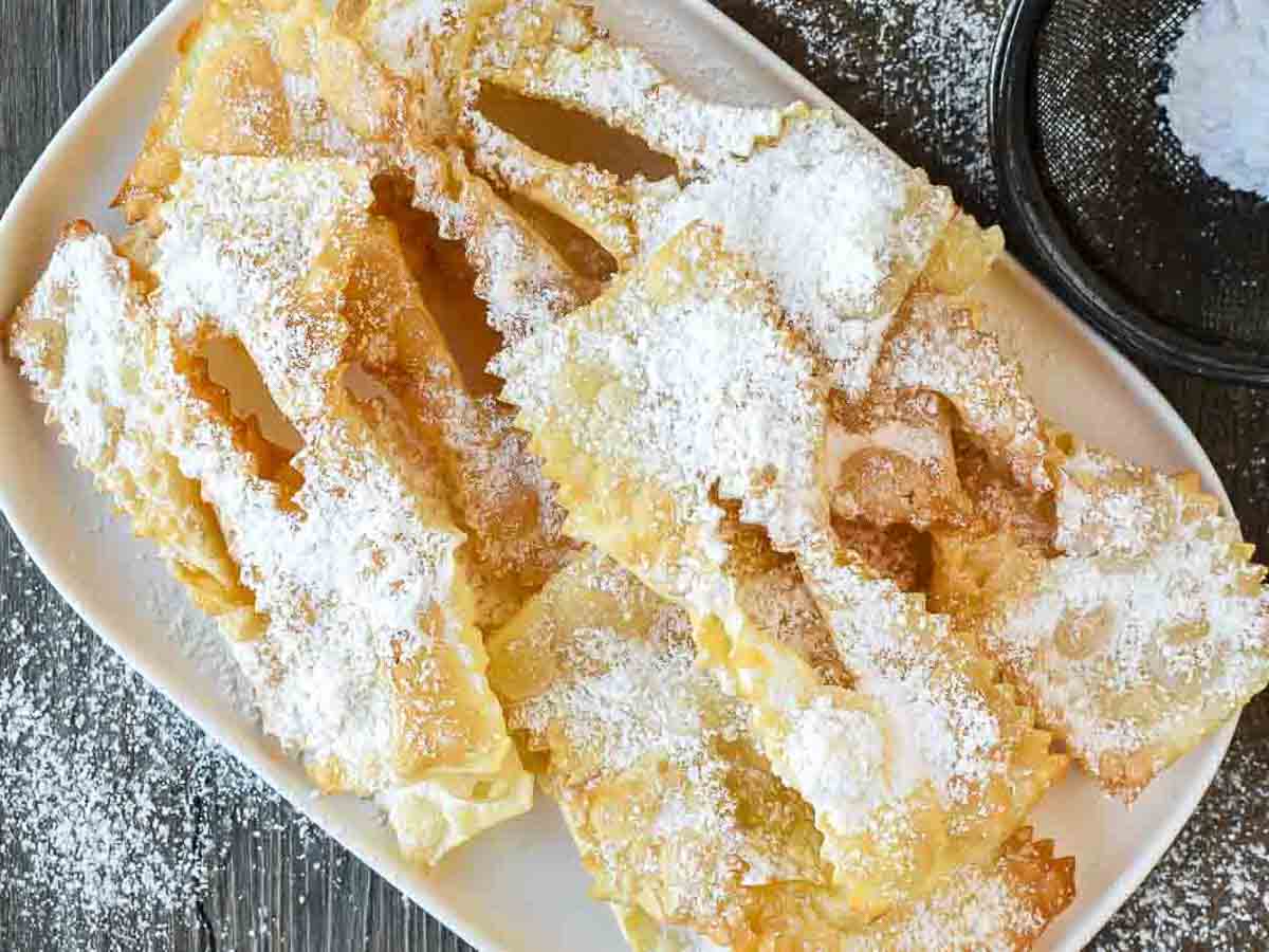 Crostoli are a crispy fried Italian pastry that is popular during Carnevale and many other celebrations. Try stopping at just one - impossible! #crostoli #angelwings #Italianfritters #easter #christmasrecipes #lent #Italiancookie #italianrecipes Fried Italian pastries dusted with powdered sugar viewed from above.