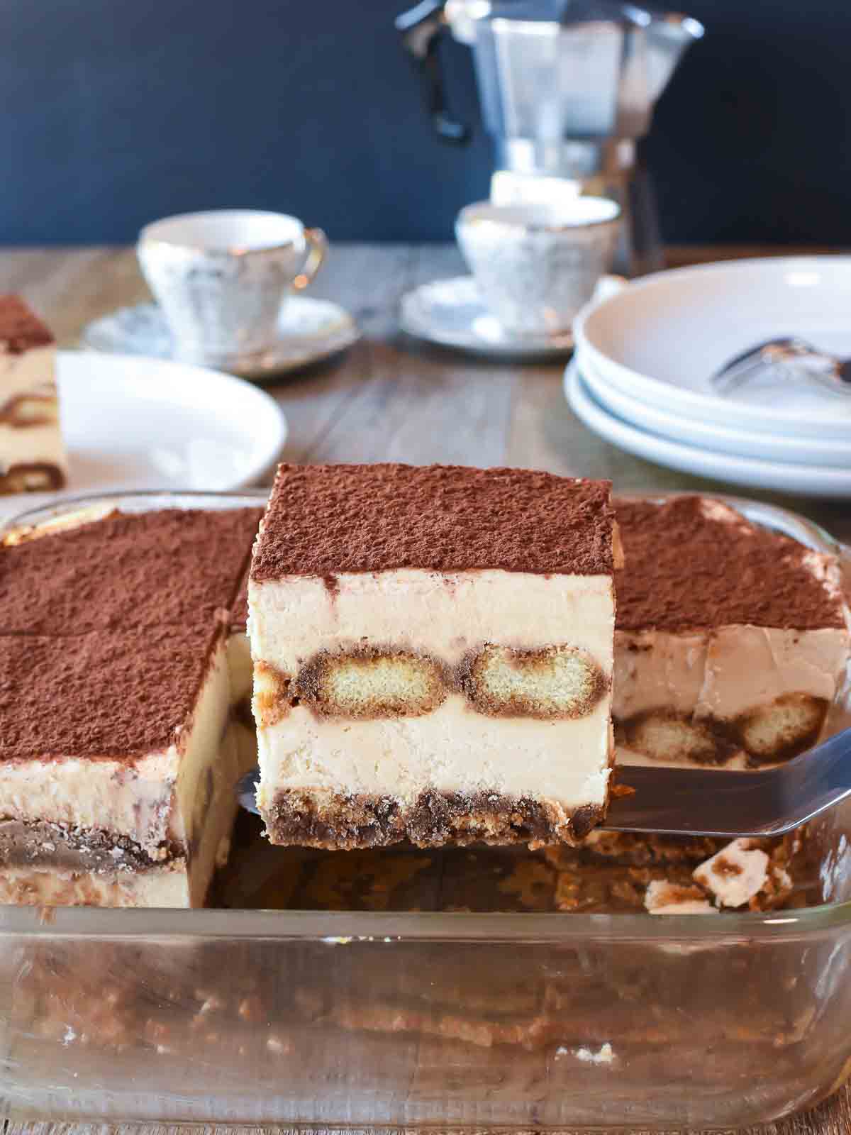 Tiramisu is a much loved Italian dessert. But do you know how to make tiramisu at home? Follow my recipe for delicious results! #tiramisu #dessert #italian #cream #nobake #tiramisurecipe #italiandessert Cross section of creamy dessert topped with cocoa powder of lifted from serving dish.