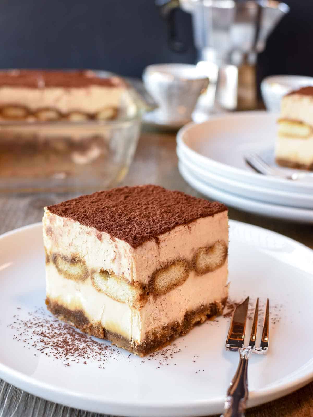 Tiramisu is a much loved Italian dessert. But do you know how to make tiramisu at home? Follow my recipe for delicious results! #tiramisu #dessert #italian #cream #nobake #tiramisurecipe #italiandessert Square slice of Italian tiramisu on white plate.