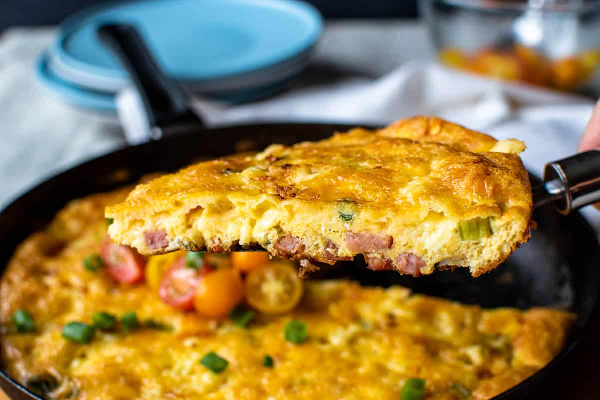Wedge of frittata being lifted out of black pan.