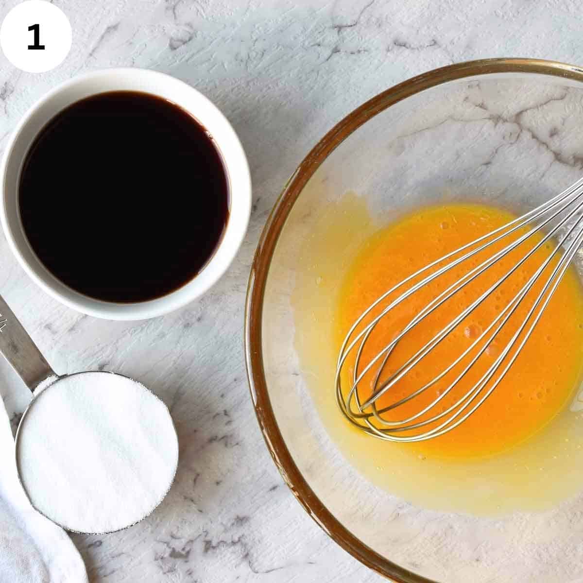 Beaten egg yolks in a glass bowl with dark wine in a small bowl and sugar in a measuring cup.