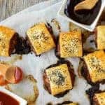 sausage rolls on baking paper with black sauce and red sauce viewed from above with text above the image