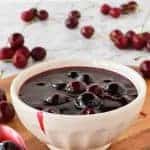 Cherry sauce in white bowl with cherries scattered around, spoonful of sauce beside bowl