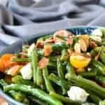 green bean salad with tomatoes and feta in blue bowl on wooden board