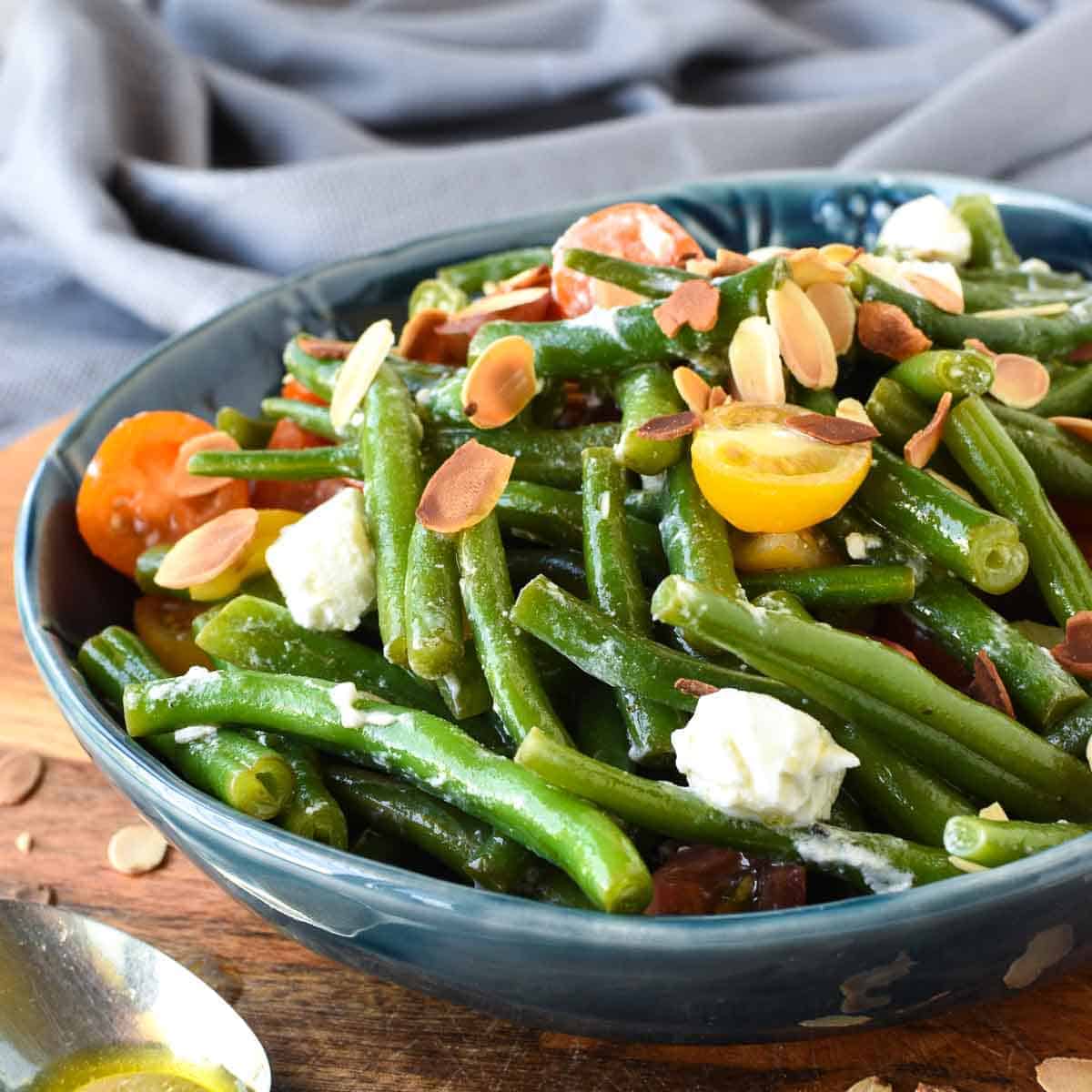 green bean salad with tomatoes and feta in blue bowl on wooden board