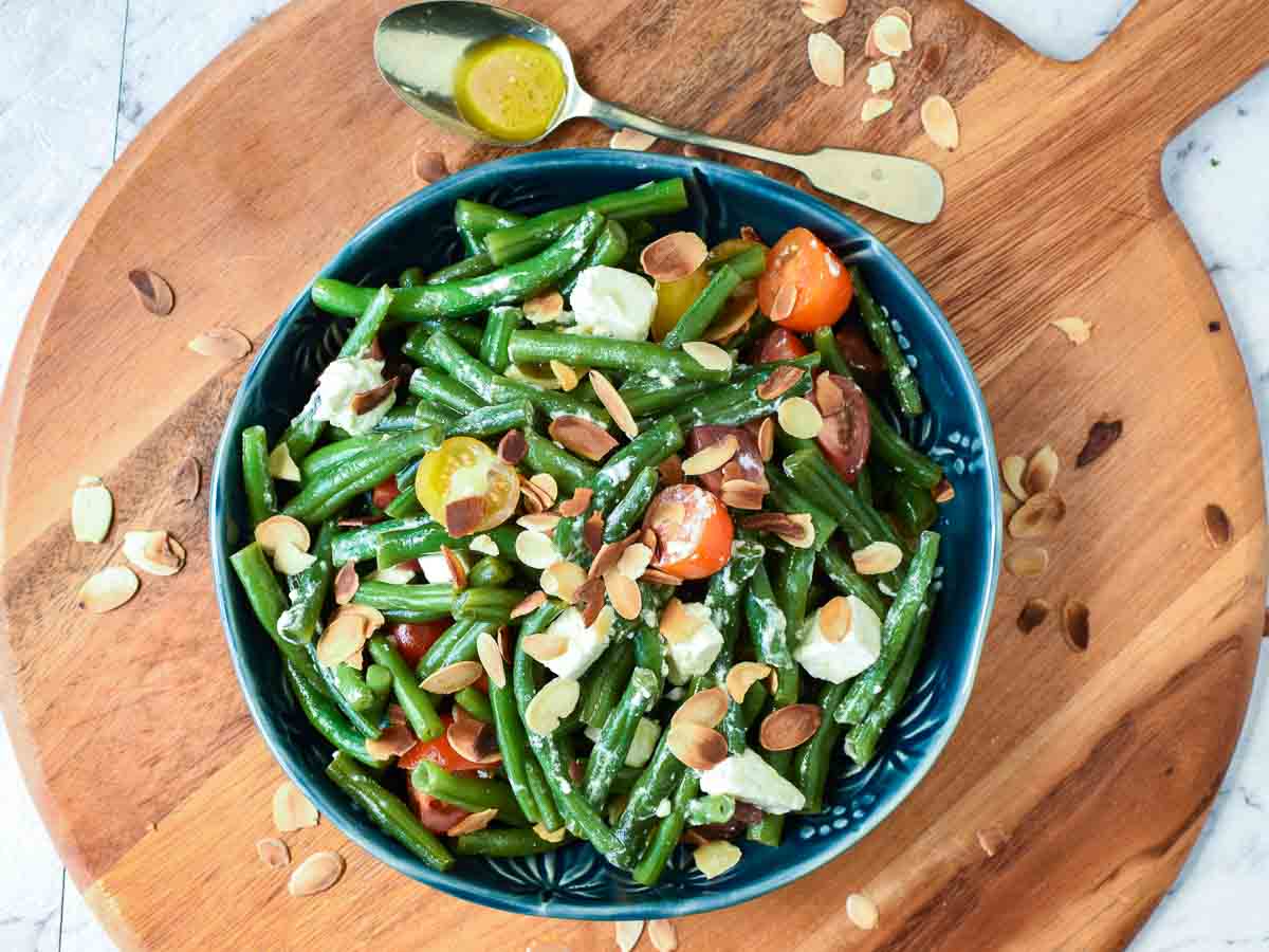 Bowl of green beans on a round wooden board viewed from above.