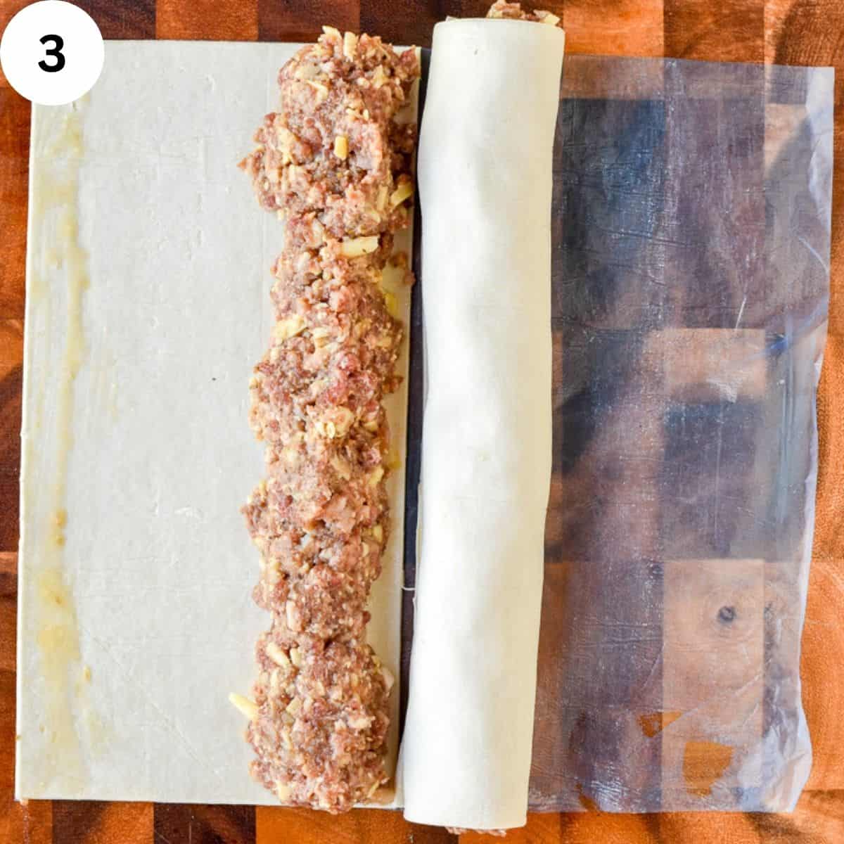Dough rolled up around filling and another rectanglar piece of dough with meat filling heaped down one side.