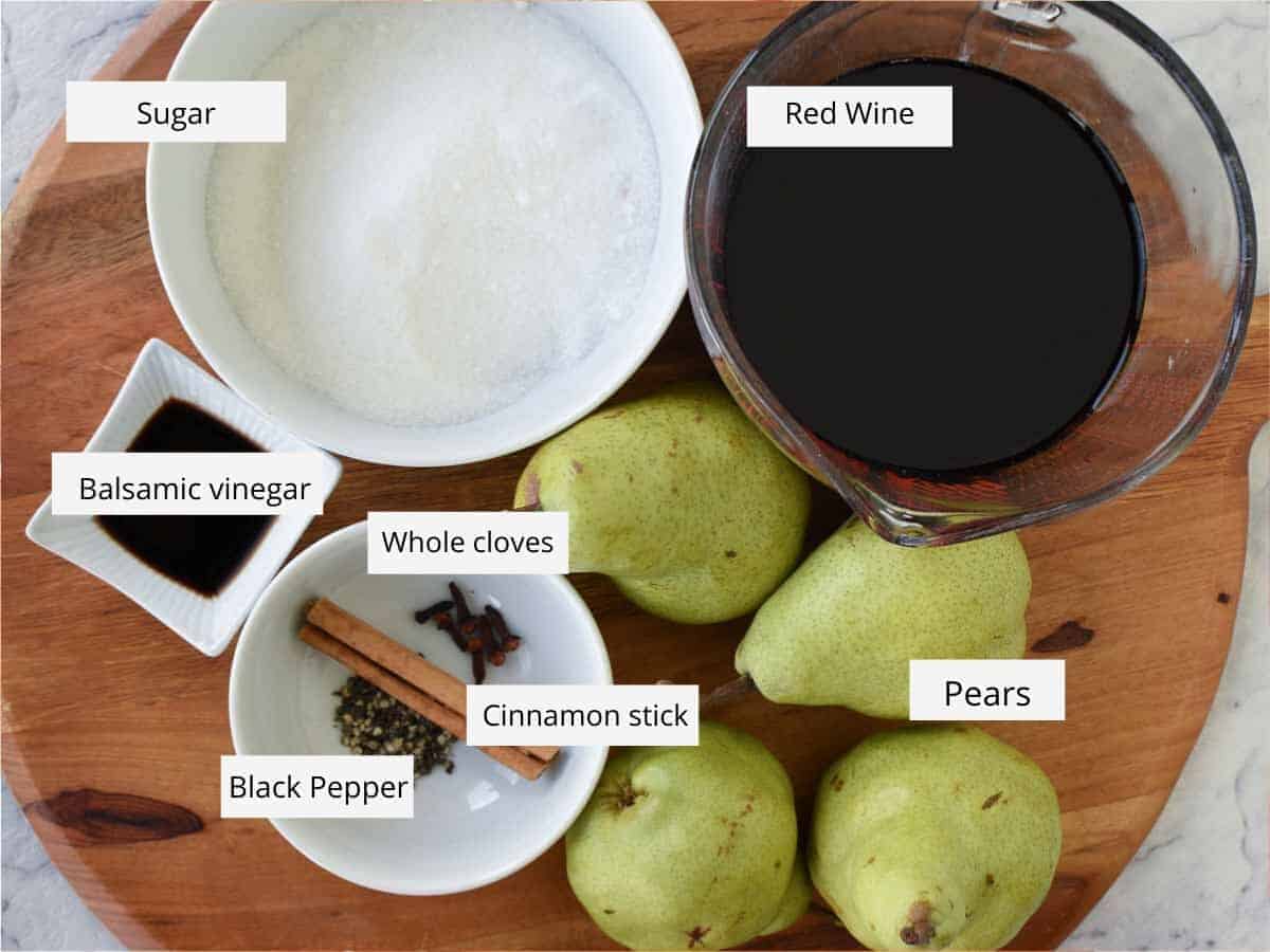 Poached Pears in Red Wine and Spices is a simple and impressive dessert that is equally at home at a dinner party or family meal. These delicious pears glisten with syrup and are fragrant with spices. Included is a special ingredient that balances out the sweetness. #pears #pearrecipe #redwine #dessert #recipe #poachedpears The Ingredients for the recipe prepared on a wooden cutting board