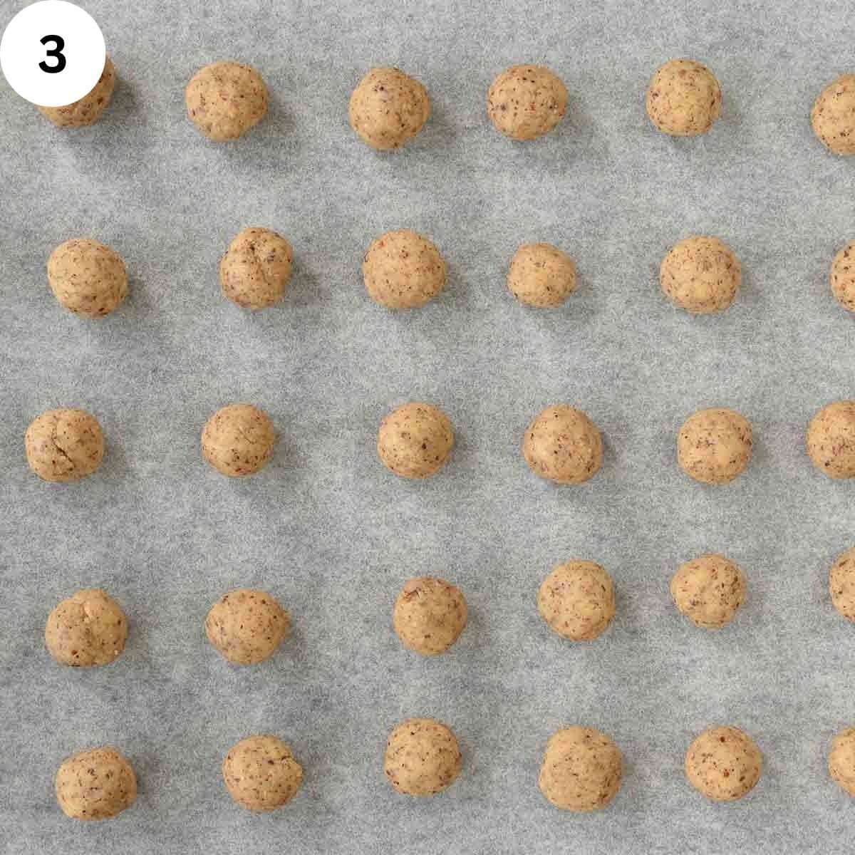 Rolled balls of cookie dough on a baking sheet.
