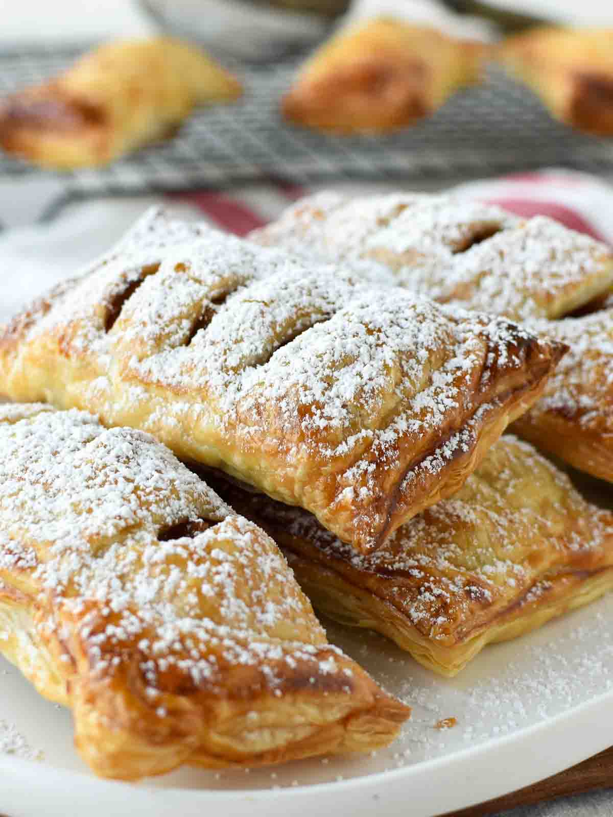 These homemade Apple Turnovers made with puff pastry are so easy. This recipe is really simple to make using store bought dough and a fresh apple pie filling. Enjoy bakery style, flaky pastries that you have baked yourself! #apple #appleturnovers #puffpastry #homemade #pies #pastry #applepies Puff pastry apple turnovers dusted with powdered sugar.