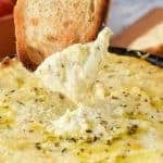 baked ricotta in black enamel pan on grey cloth with a slice of toasted bread dipping in