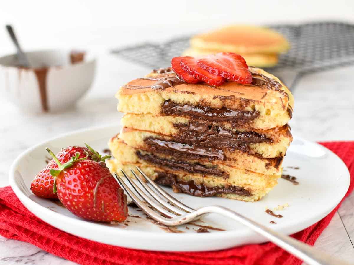 Makes 8 Nutella Stuffed Pancakes. Not just for breakfast, these Pancakes Stuffed with Nutella make a decadent snack or dessert. You'll love how easy this fluffy pancake recipe is! #pancakes #homemade #nutellapancakes #nutella Stack of halves pancakes with melted chocolate inside.