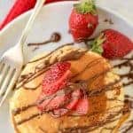 pancake stack drizzled with chocolate and decorated with strawberries on a white plate viewed from above