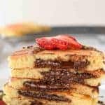 five stacked nutella filled pancakes on white plate sliced in half showing the nutella oozing out