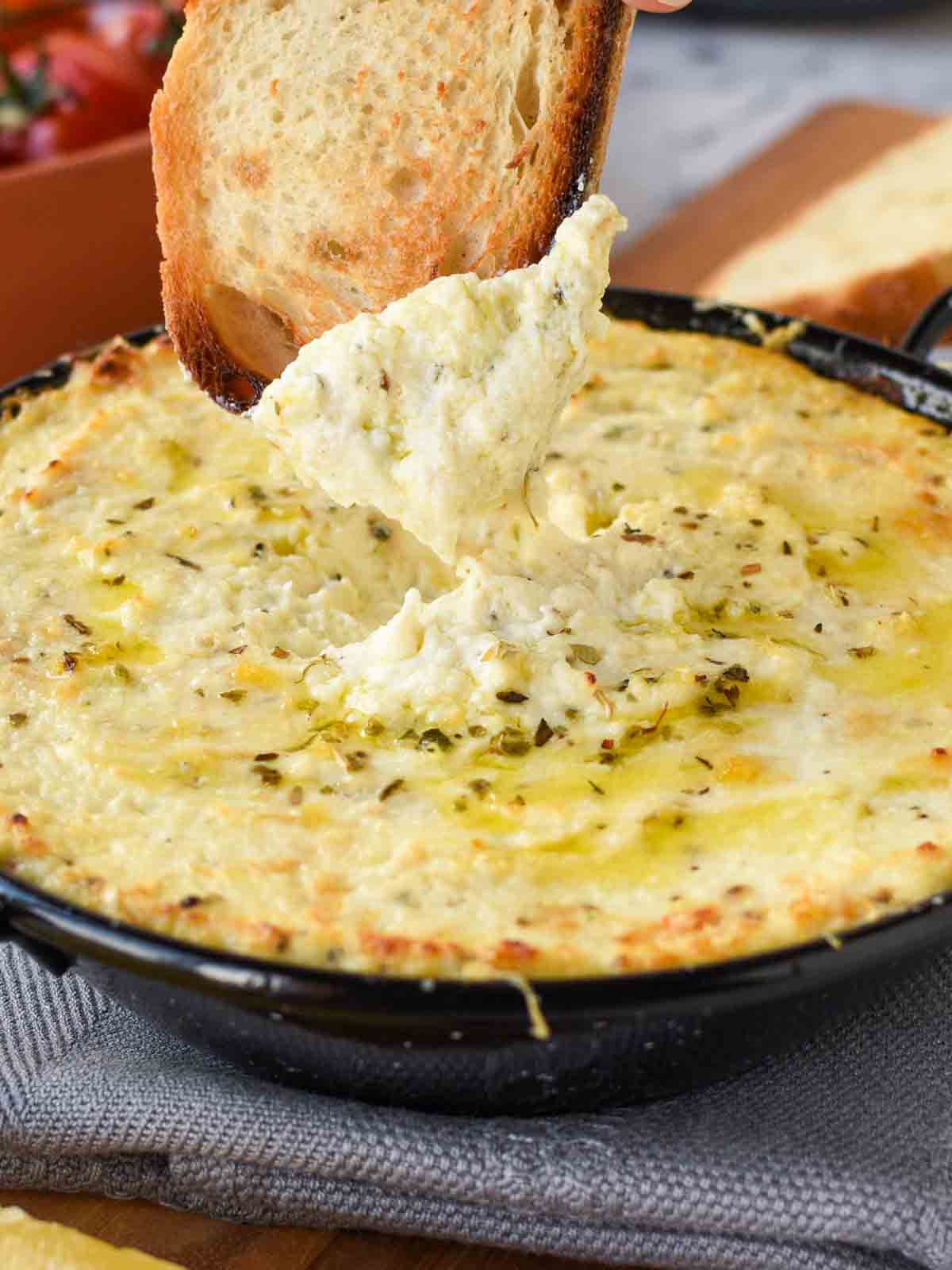 30 minutes. Serves 8. This Creamy Baked Ricotta Dip is full of lemon and garlic flavours. Serve with Roasted Tomatoes and crusty bread for a delicious, savory appetizer. baked ricotta in black enamel pan on grey cloth with a slice of toasted bread dipping in.