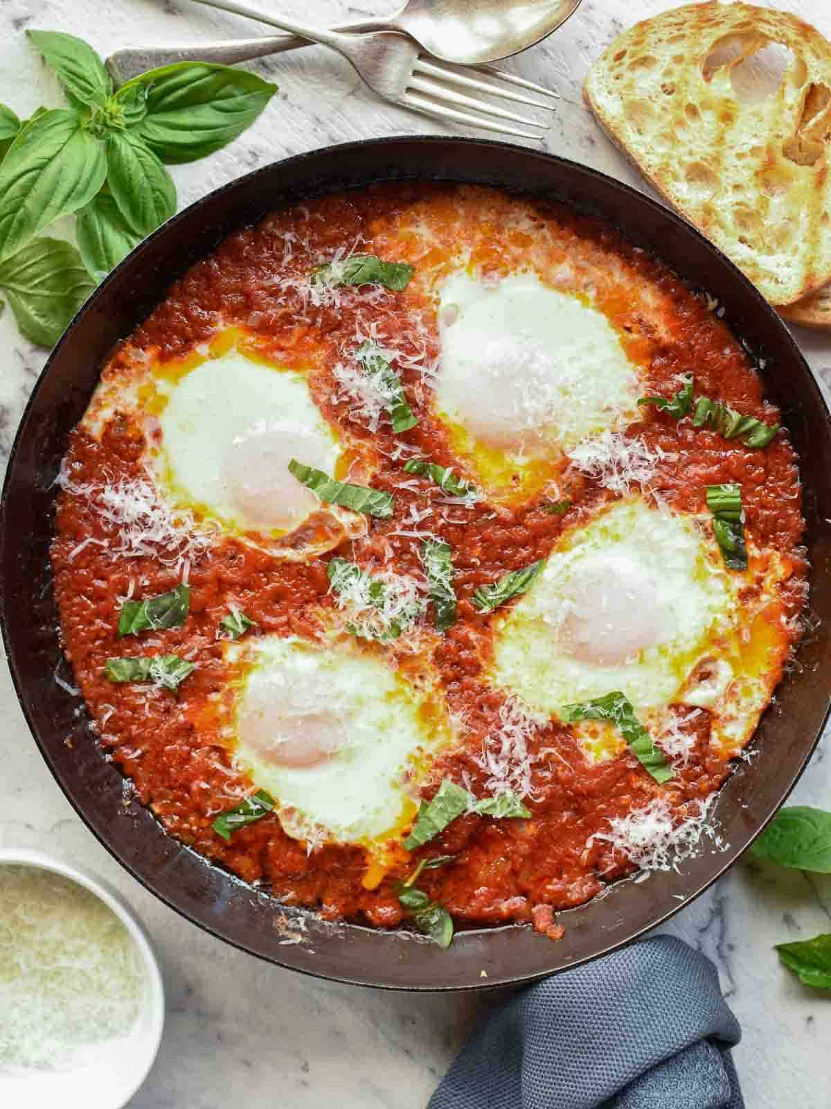 Eggs in Purgatory is an easy Italian dish you can prepare in less than 30 minutes. Eggs are poached in a spicy tomato sauce until the whites are set and the yolks are still creamy. Pure comfort food! #Italian #recipes #comfort #food #eggs #easyrecipe #eggsinpurgatory four poached eggs in tomato sauce in black pan viewed from above.