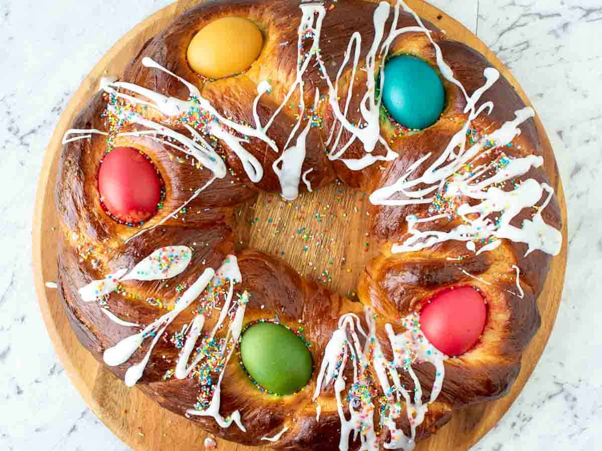Baked bread in ring shape, decorated with dyed eggs and drizzle of icing, viewed from above.