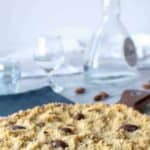 Text reads Italian Crumble cake Traditional recipe. image of crumbly large cookie cake on white paper doily, glasses and bottle in the background