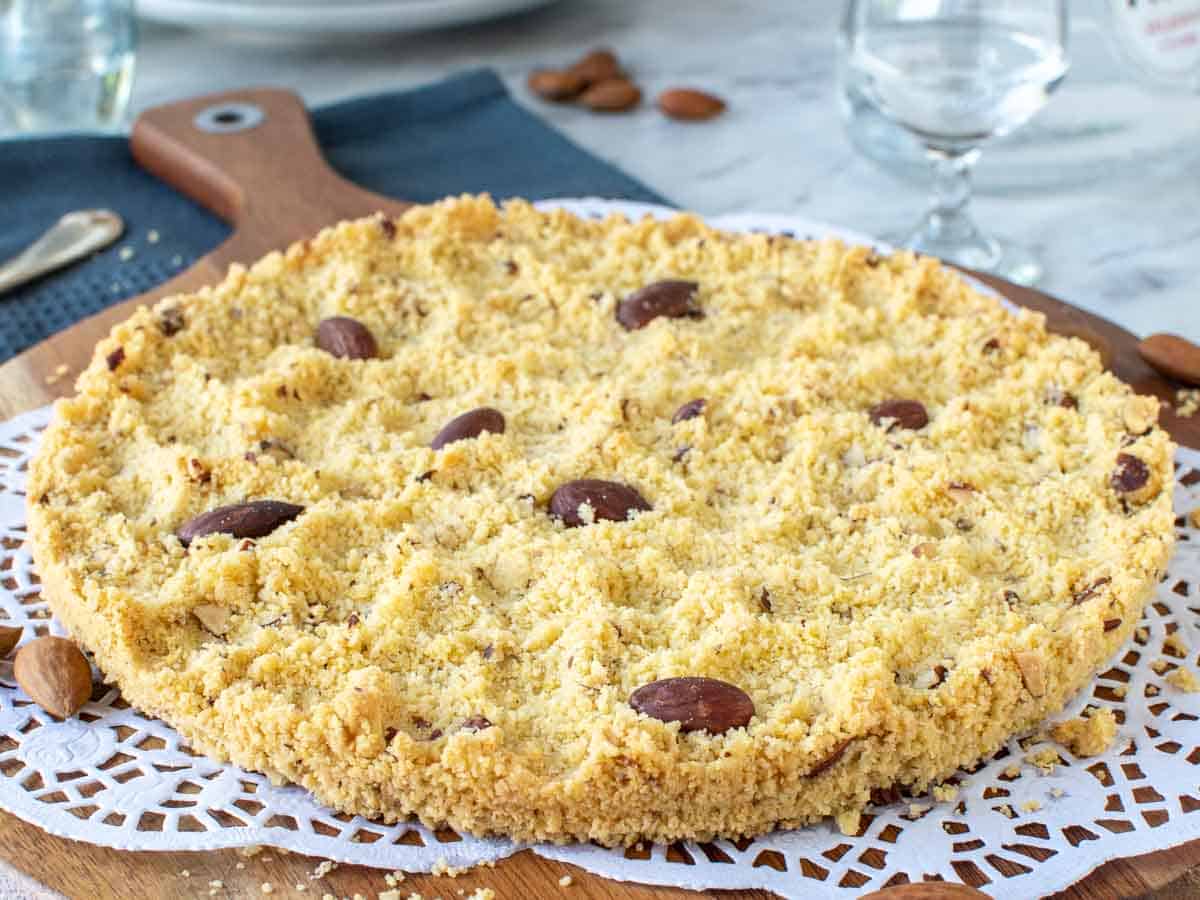 Whole crumbly cake on wooden board and white paper doily.