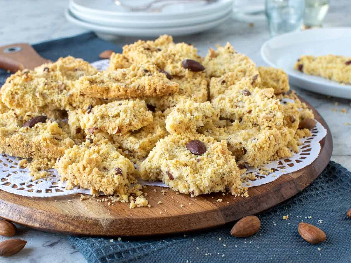 Uneven pieces of crumbly cake stack up on wooden board and white paper doily.