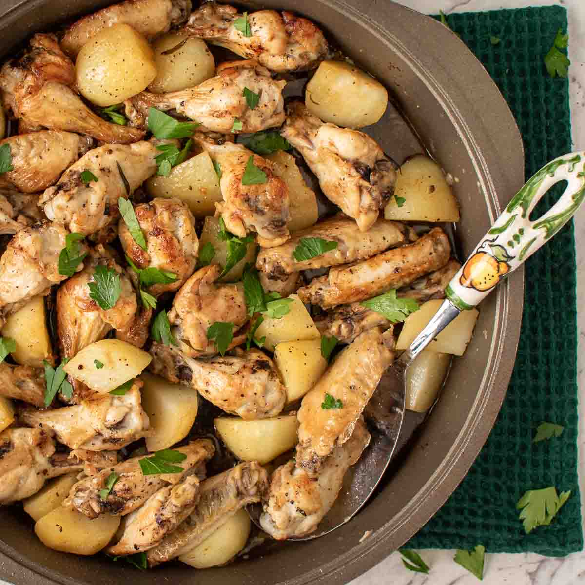 close up of braised chicken wings with potato chunks sprinkled with chopped parsley viewed from above
