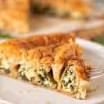 slice of spinach ricotta filo pie on white plate with fork piercing the edge