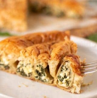 slice of spinach ricotta filo pie on white plate with fork piercing the edge