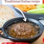 Image with text. Text reads Bagna Cauda traditional Italian recipe. Image is Bagna cauda sauce in a black dish surrounded by sliced vegetables and bread