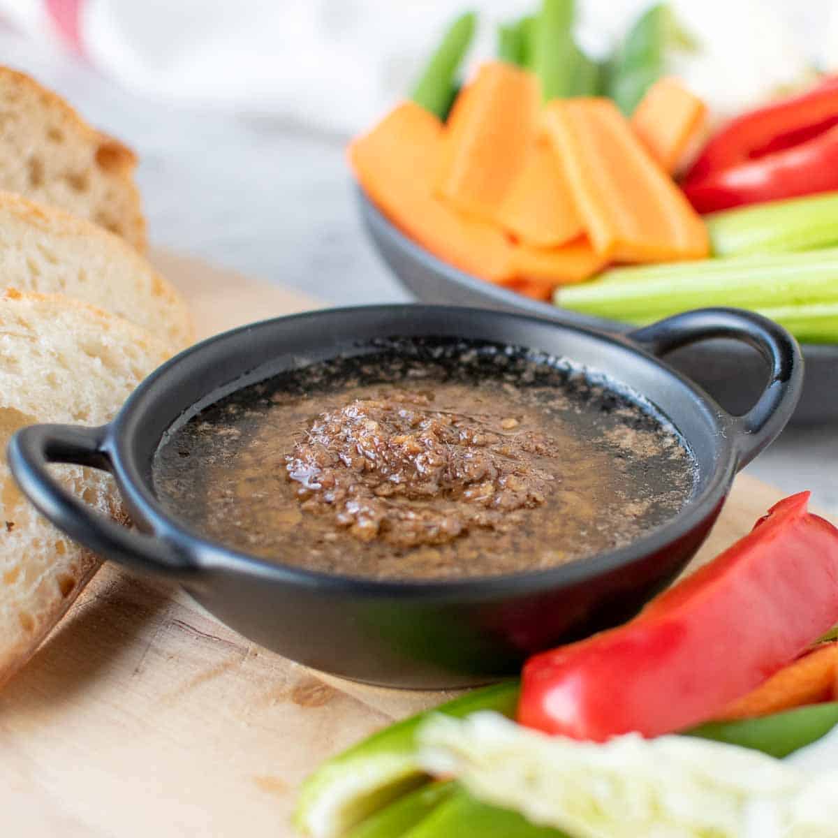 Bagna cauda sauce in a black dish surrounded by sliced vegetables and bread
