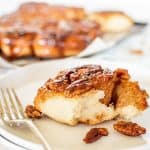 a sticky pecan bun on white plate and whole bun in the background