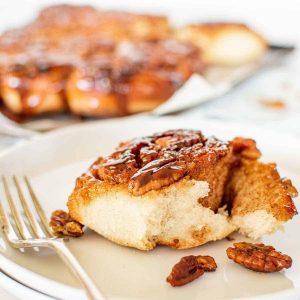 a sticky pecan bun on white plate and whole bun in the background