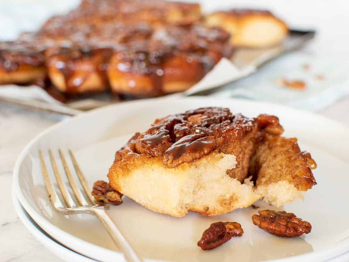 A caramel cinnamon roll on white plate and whole bun in the background.
