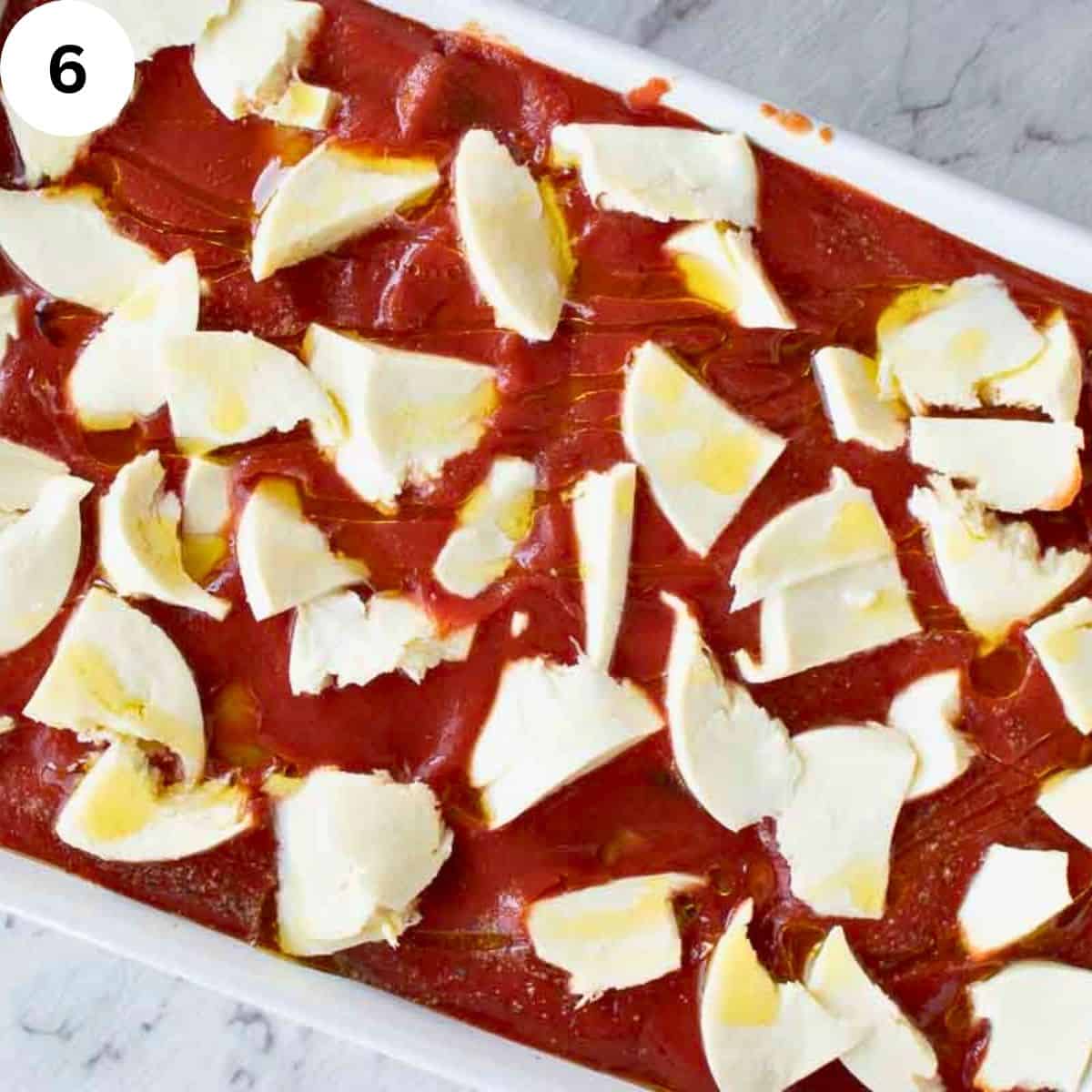 Overhead view of tomato puree in a baking dish topped with chopped cheese.