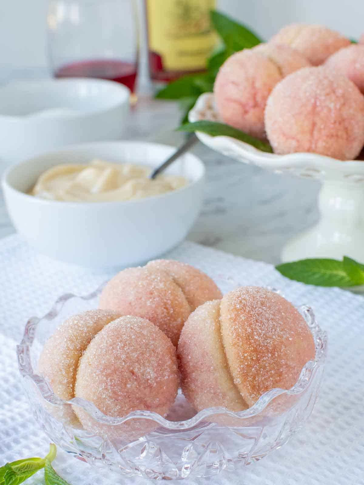 Three Italian peach cookies in glass bowl with more cookies in the background.