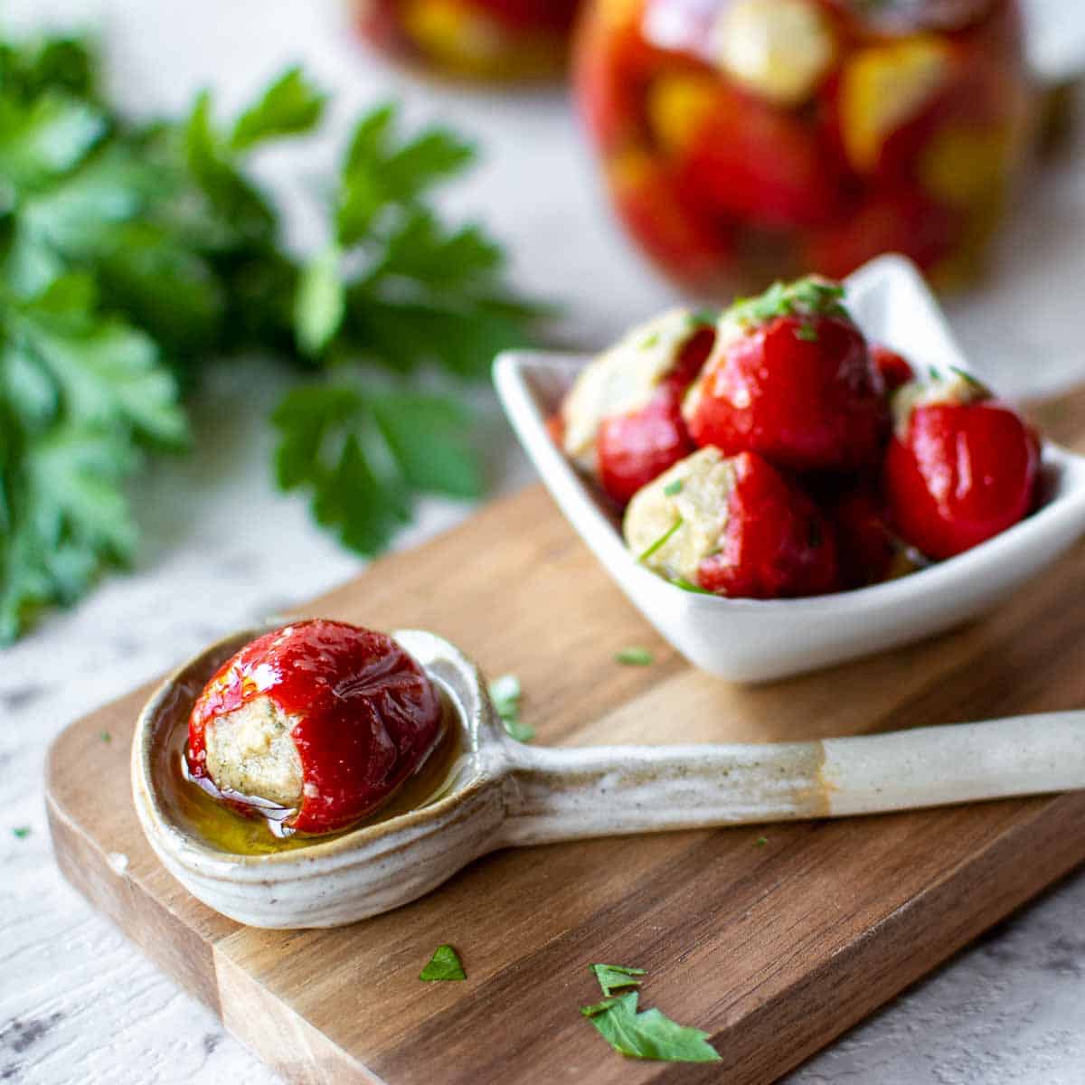 one stuffed cherry pepper in a spoon and pile of stuffed cherry peppers in a white dish with bottles filled in the background