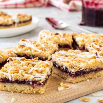 Raspberry bars on wooden board with jam and extra bars in the background.