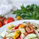 cucumber tomato onion salad on white plate with tomatoes and parsley in the background