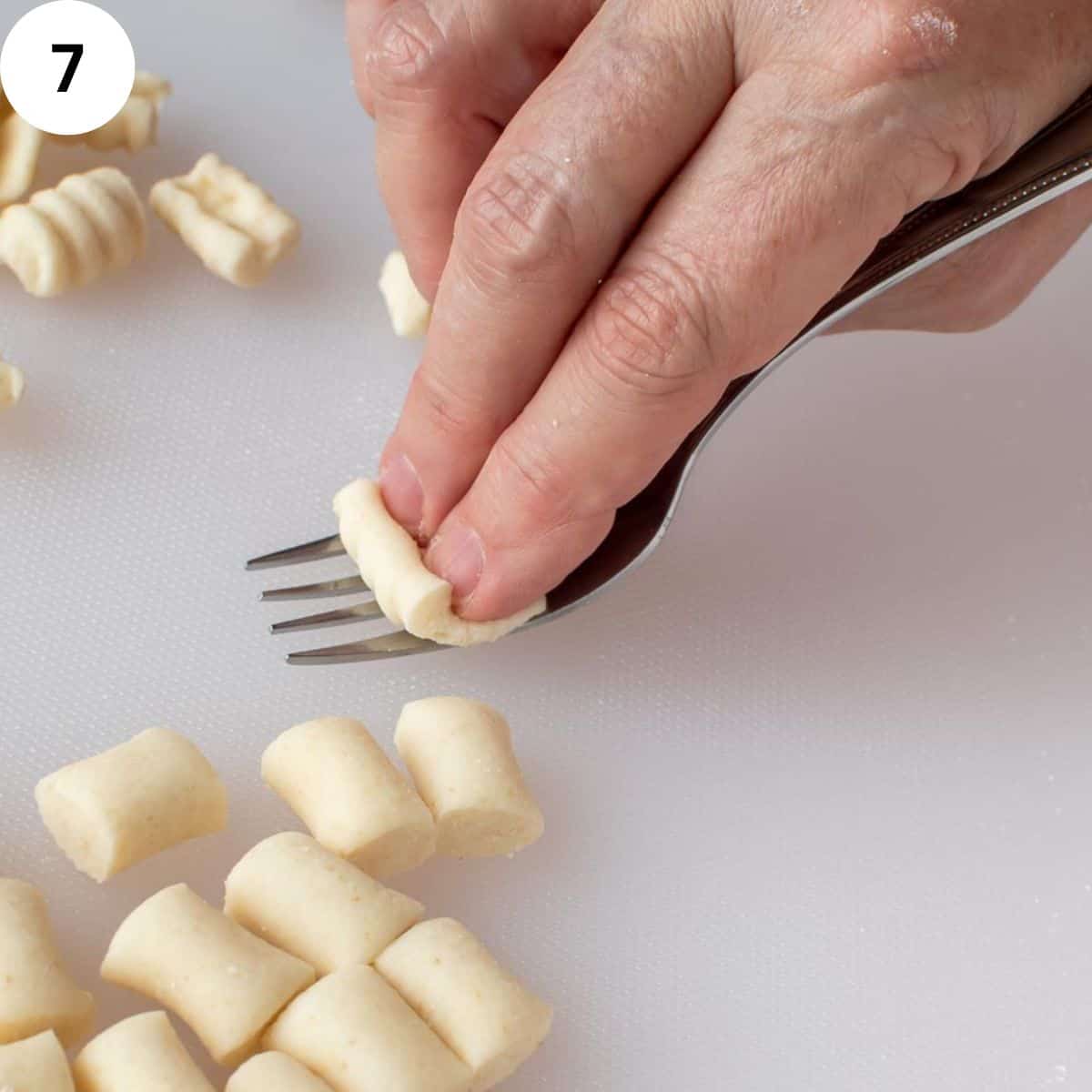 Two fingers using the tynes of a fork to shape pasta dough.