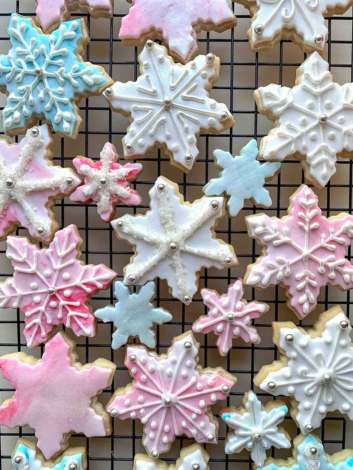 Decorated snowflake cookies on black wire rack viewed from above.